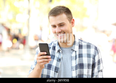 Happy boy walking and reading messages on the phone on the street Stock Photo