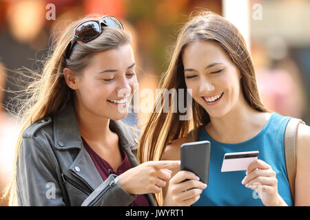Two happy friends buying on line with credit card and smart phone on the street Stock Photo
