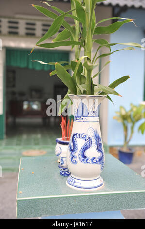 Close up of vase and incense outdoors with backdrop of Vietnamese style home in Lai Thieu. VIETNAM Stock Photo