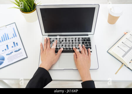 High angle view of unrecognizable businesswoman typing on laptop keyboard, notepad and documents lying on office desk Stock Photo