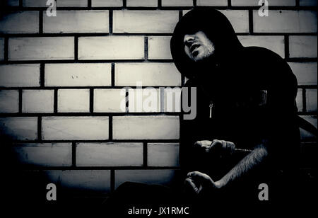 black and white portrait of young sick drug addict man wearing hood holding heroin or cocaine syringe. Boosted contrast to make the darkness of the ph Stock Photo