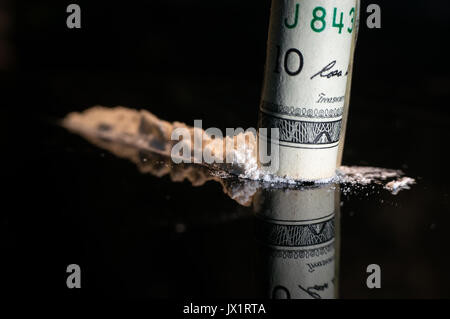 Snorting a line of cocaine. There are three lines on a glass table. snorting through a rolled bill. Focus on the bill. Stock Photo