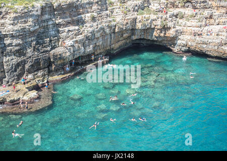 Swimmers wade into the spectacular turquoise ocean at Polignano A Mare. The beach is also the site of the annual Red Bull cliff-diving competition. Stock Photo