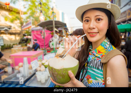 woman holding coconut water standing on the Thailand famous outdoor street smiling taking beautiful photo at the Chatuchak Weekend Market in the Asia  Stock Photo