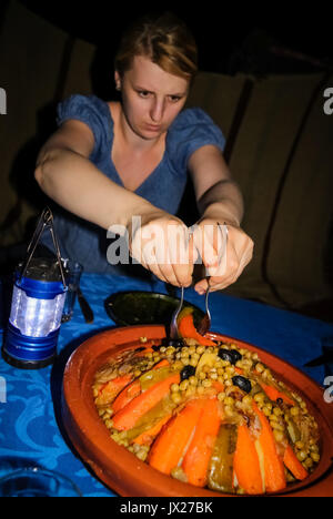 Female Caucasian tourist using forks to take portion of Tajine - traditional Moroccan meal Stock Photo