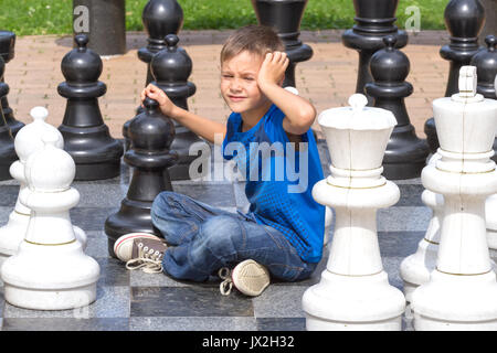 Chess game with giant chess piece. Boy playing strategic outdoor game on black and white board Stock Photo