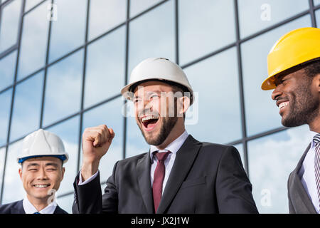 multiethnic group of excited professional architects in helmets outside office building, architects meeting concept Stock Photo