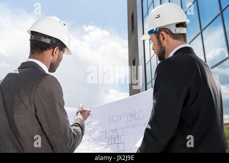Back view of professional architects in hardhats working with blueprint Stock Photo