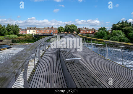 A footbridge crossing a river with a weir to th side. Stock Photo