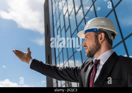 Professional architect in hard hat wearing suit and gesturing outside Stock Photo