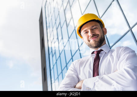 portrait of smiling professional architect in hard hat against building  Stock Photo