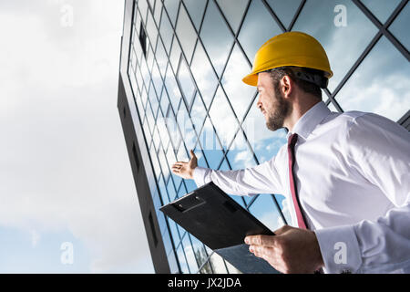 side view of professional architect in hard hat holding folder and gesturing Stock Photo