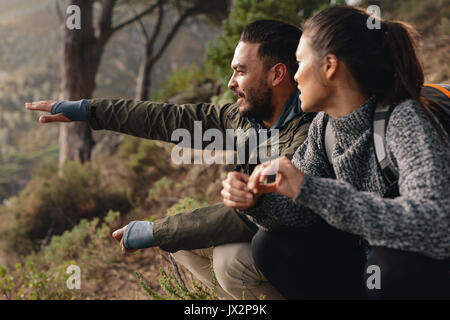 Young couple relaxing, with man showing something to woman. Young couple hiking on mountains. Stock Photo