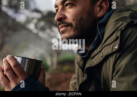 Close up shot of young caucasian man holding coffee, taking break during hiking. Male hiker taking rest outdoors. Stock Photo