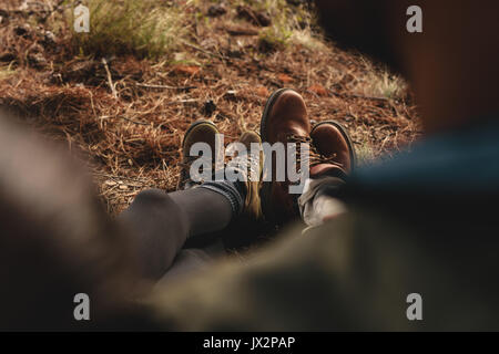 Close up of couple of hikers sitting together outdoors, focus on legs. Hikers resting on country trail. Stock Photo