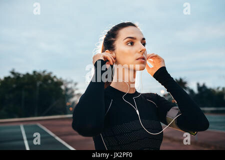 Outdoor shot of beautiful young sportswoman with earphones on tennis court. Caucasian fitness female in sportswear. Stock Photo