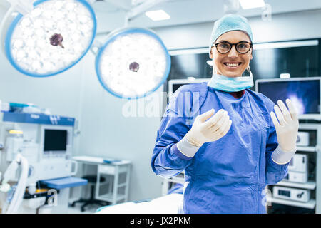 Portrait of happy woman surgeon standing in operating room, ready to work on a patient. Female medical worker in surgical uniform in operation theater Stock Photo