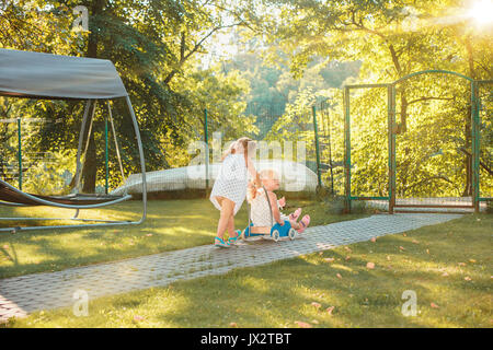 Cute little blond girls riding a toy car in summer. Stock Photo