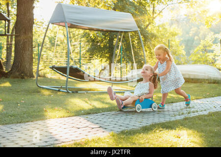 Cute little blond girls riding a toy car in summer. Stock Photo