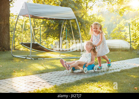 Cute little blond girls riding a toy car in summer. Stock Photo