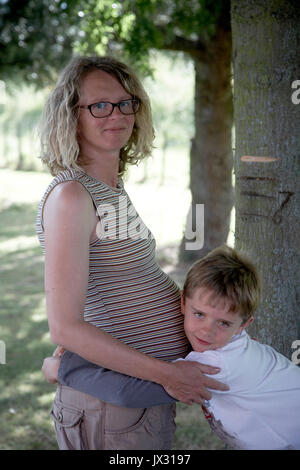 Elder brother with pregnant mum hugging bump Stock Photo