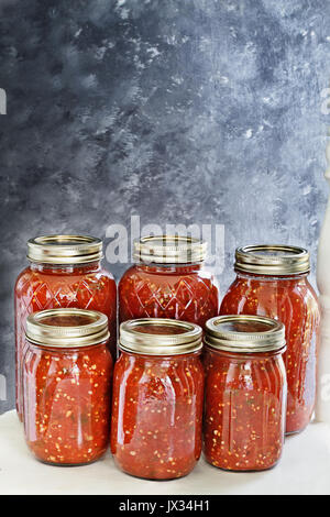 Mason jars canned with homemade salsa sitting on an old white country chair in front of a dark background. Shallow depth of field with selective focus Stock Photo