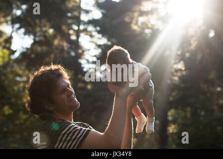Happy joyful father having fun throws up in the air his child in the park in the evening - intentional sun glare and vintage color, lens focus on father. Father's day. Film filter Stock Photo