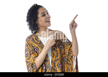 Girl is pointing fingers in the same direction. She smiles and seems to be excited. Short and curly haired woman wears yellow clothes and with floral  Stock Photo