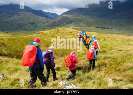 People wearing raingear on Carnedd y Cribau trekking down to Pen Y Gwryd in sunshine following wet weather rain in mountains of Snowdonia. Wales UK