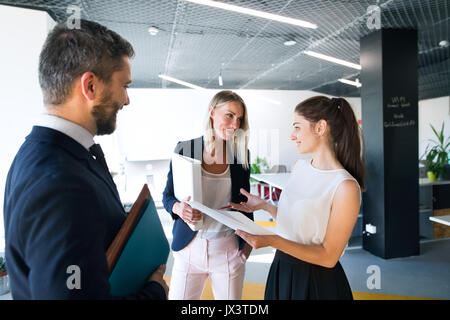 Three business people in the workplace. Two women and man standing in the office talking together. Stock Photo