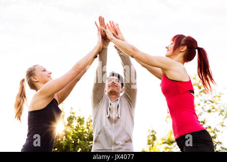 Group of young runners in park giving high five after completing exercise. Teamwork gesture. Stock Photo