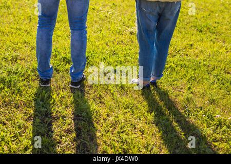stylish couple legs on sunny grass in meadow in summer, travel together concept, space for text. Stock Photo