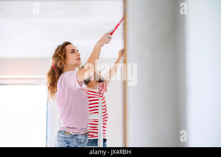Beautiful young couple painting walls in their new house using paint brushes. Home makeover and renovation concept. Stock Photo