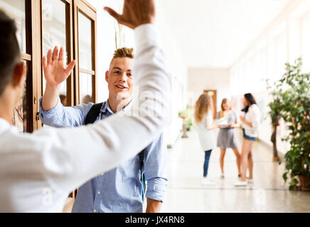 Two handsome teenage students in high school hall giving high five. Stock Photo