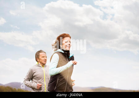Beautiful active senior couple running outside on green hills. Stock Photo