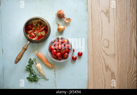 Vintage set of fresh homemade cherry tomato salsa, fresh homemade carrots and parsley cooked in old copper pot, placed on rustic wooden table. Stock Photo