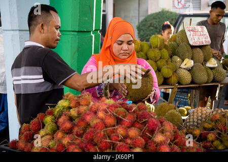 Kota Kinabalu, Malaysia - August 1, 2017: Customer choosing a fruit to buy at the fruit stall in Kota Kinabalu night market, Sabah Borneo. Stock Photo