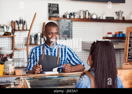 Smiling barista talking to a customer in his cafe Stock Photo