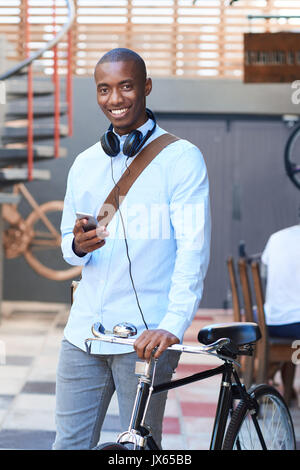 Smiling man standing with his bike using a cellphone Stock Photo