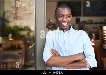 Young African entrepreneur leaning on the door to his cafe Stock Photo