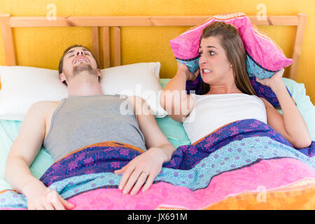 Woman is sleepless and angry because of her snoring husband in bed Stock Photo