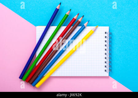 Notepad for notes and colorful pencils on colored background. Studio Photo Stock Photo