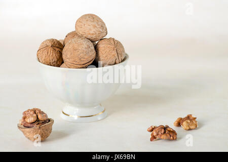 Walnut in a shell are stacked in a white cup. Next peeled nuts. Vegetable protein is an analogue of an animal. Light background Stock Photo