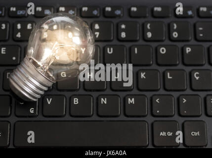 Lit light bulb lamp on top of a notebook computer black keyboard, technology concept and idea, with visible slightly out of focus keyboard letters. Stock Photo
