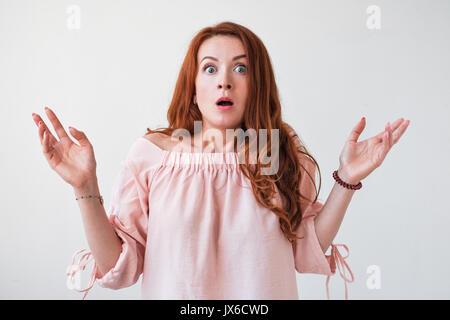 Portrait young woman with long curly red hair looking excited holding her mouth opened isolated on white wall. Stock Photo