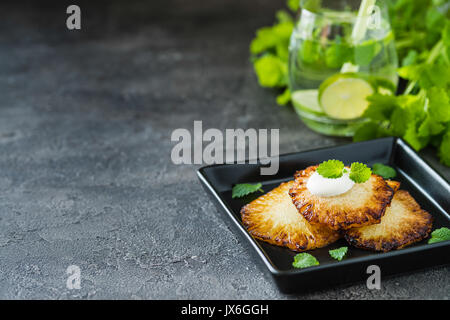 Fried pineapple slices with creme fraiche, mint on dark background. Copy space Stock Photo
