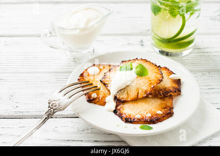 Fried pineapple slices with creme fraiche, mint in white plate on wooden background Stock Photo