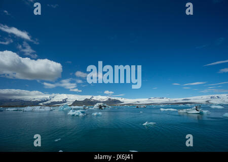 Iceland - White snow on glacier behind glowing icebergs and tourist boat far away Stock Photo