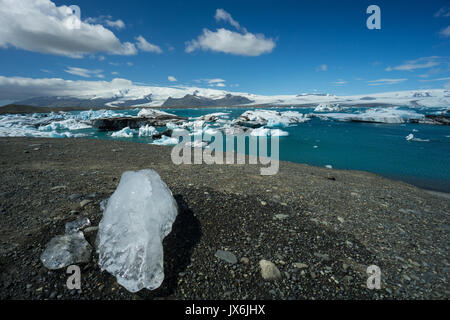 Iceland - Melting peace of ice on hill next to blue glacial lake Stock Photo