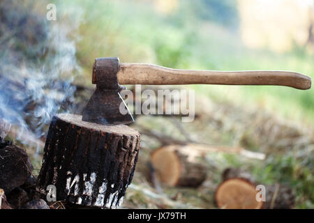 Axe in tree stump and smoke from campfire in morning at summer forest Stock Photo